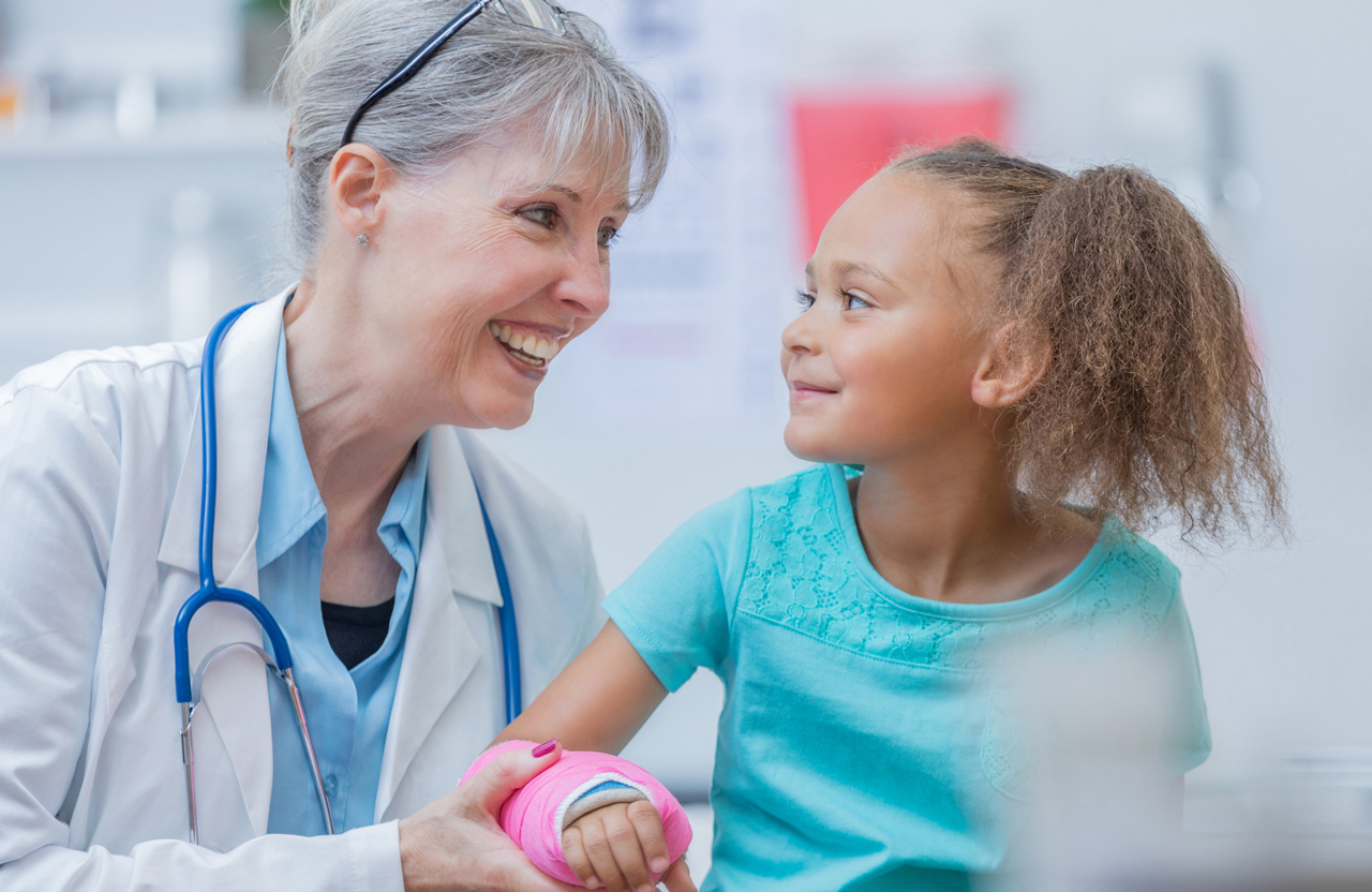 Medical professional talking with a young patient who is wearing a cast on her right forearm.