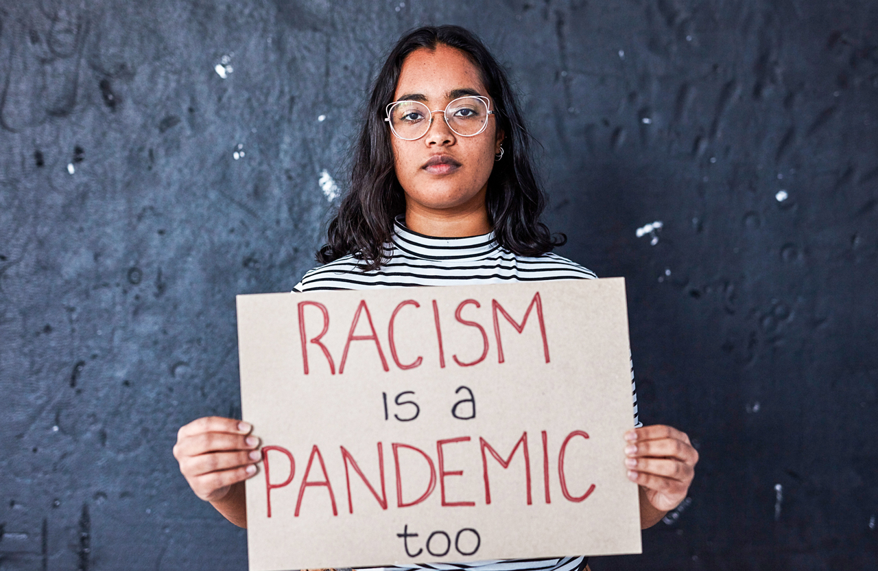 Young woman holding a sign that says "Racism is a pamdemic too."