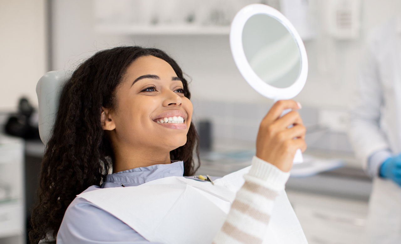 Woman admiring her newly-whitened teeth in a mirror.