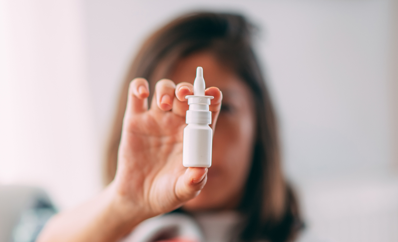 Woman holding nasal spray dispenser in front of her face.